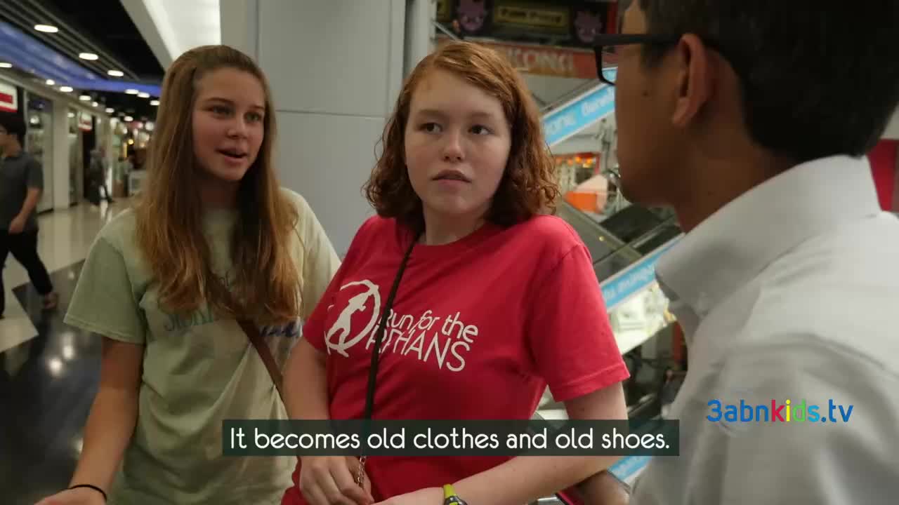 Two young women, one in a red "Run for the Orphans" t-shirt, listen intently as a man in a white shirt speaks. The scene appears to be filmed in a public space, possibly a shopping mall, with the 3abnkids.tv logo visible.
