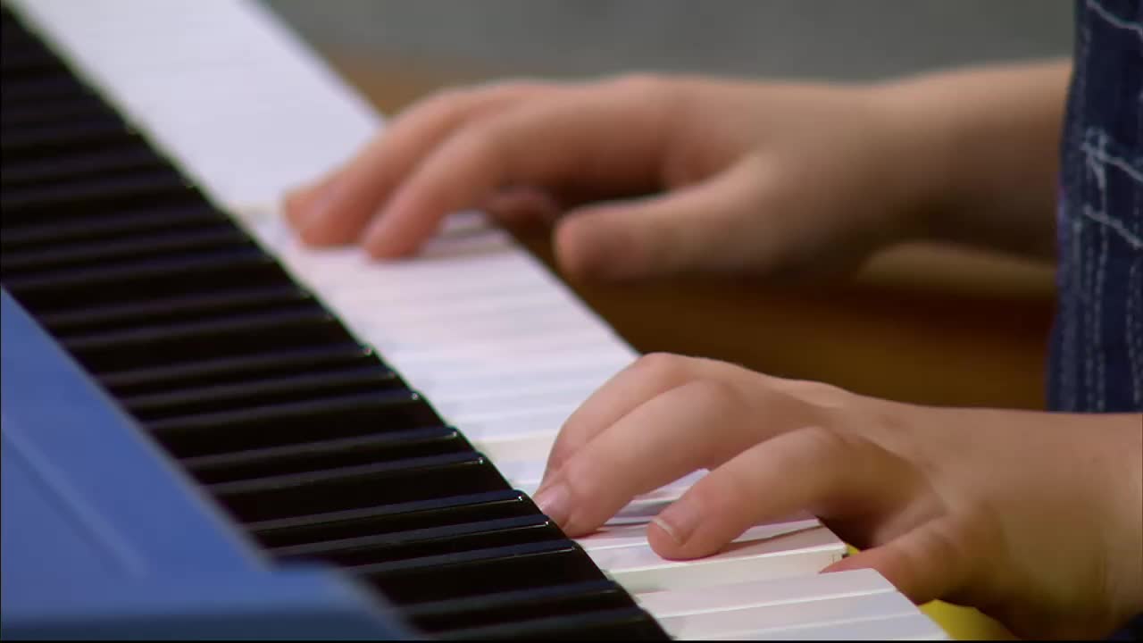 Small hands press down on the white keys of a keyboard. The fingers move with purpose, creating a melody.