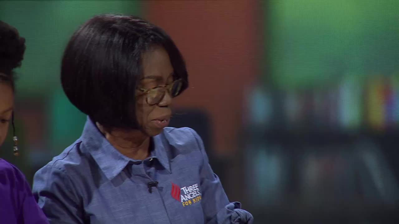 A woman with glasses and a short black bob speaks, her blue shirt bearing the "Three Angels for Kids" logo. Beside her, a young girl with braided hair looks down.