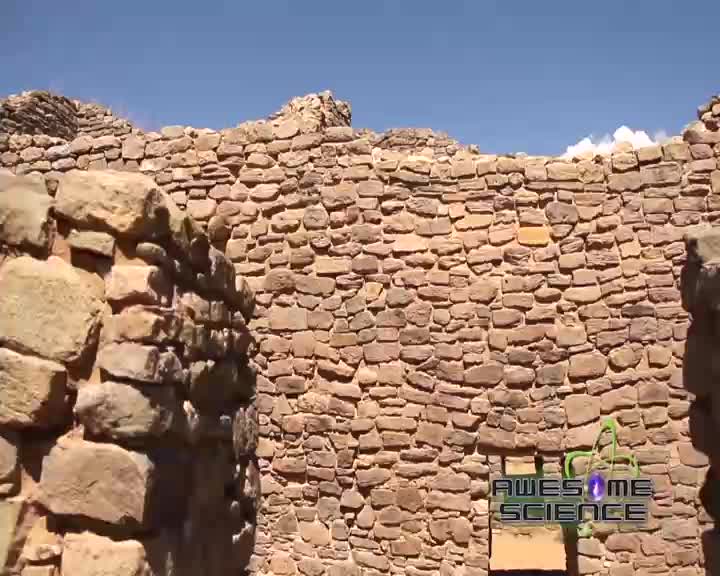 The sun beats down on ancient stone walls, their rough surfaces a testament to time. A bright blue sky stretches above the crumbling structures, hinting at a clear day in the American Southwest.