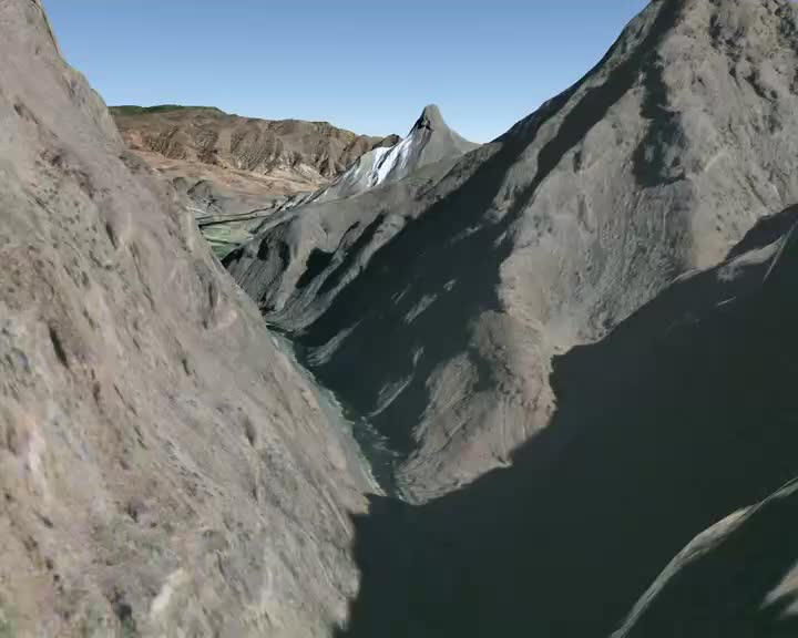 The steep, rocky walls of a canyon rise on either side, casting long shadows. A narrow river winds through the valley floor far below, disappearing into the distance.