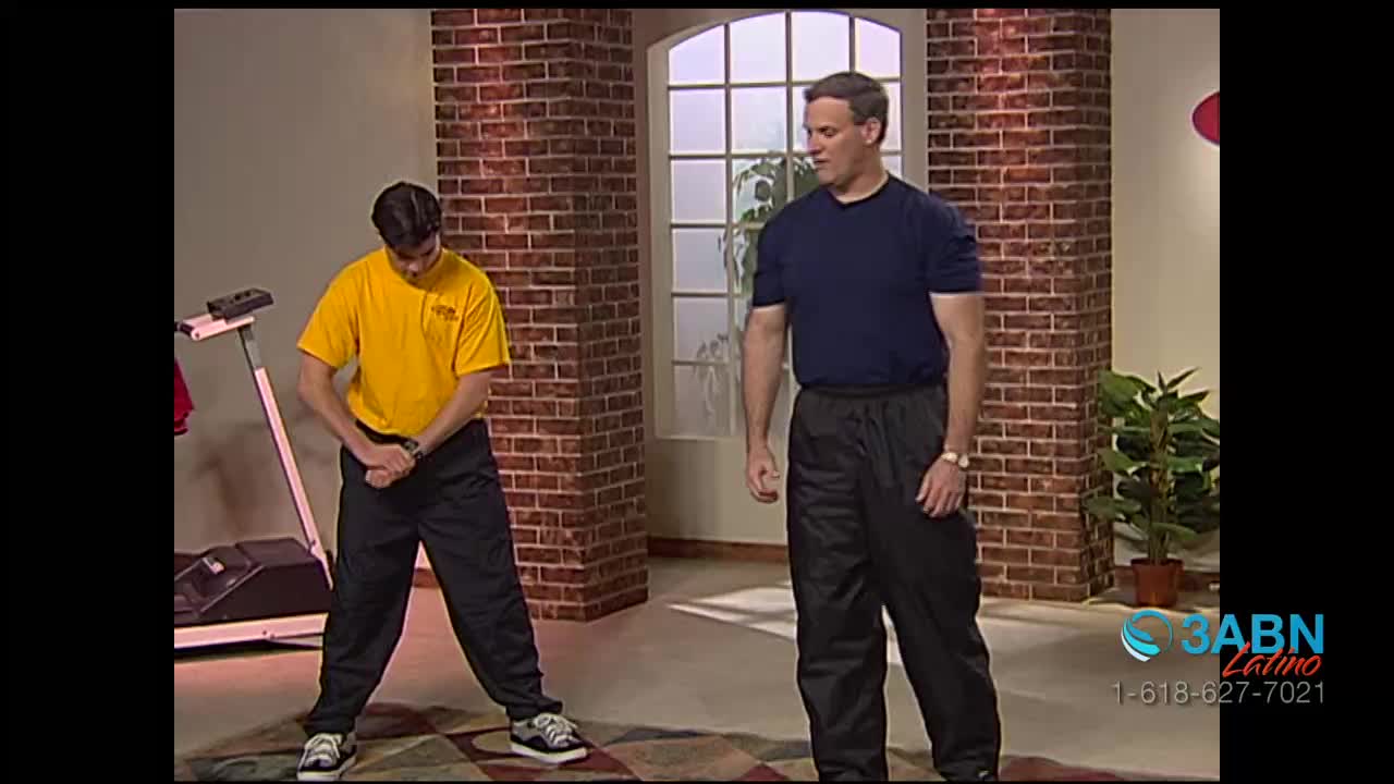 A man in a yellow shirt stretches, arms crossed in front of him, while another in a blue shirt stands nearby. The 3ABN Latino logo is visible in the corner, and a treadmill sits in the background.
