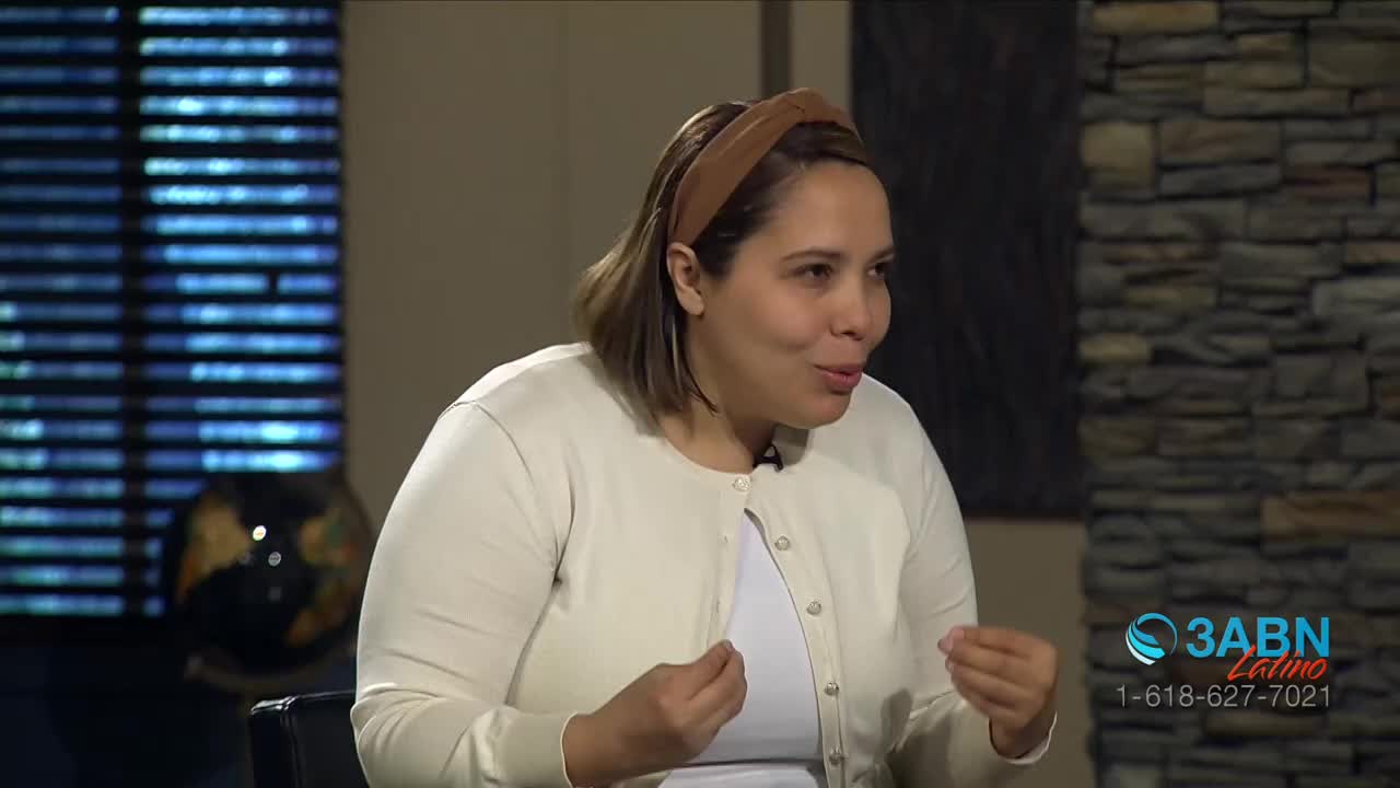 A woman in a light sweater gestures with her hands as she speaks, framed by a backdrop of blinds and a stone wall. The 3ABN Latino logo sits in the corner of the screen.

