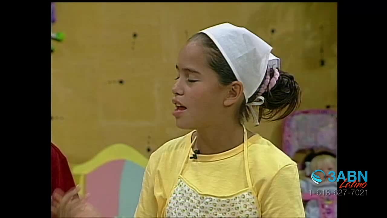 A young girl, wearing a yellow shirt, apron, and headscarf, is speaking with her eyes closed. The 3ABN Latino logo is visible in the corner of the screen.
