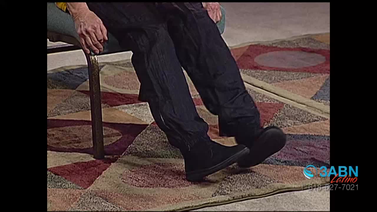 A person is seated, their legs casually extended in front of them. The black shoes rest on a patterned rug, visible beneath dark pants.
