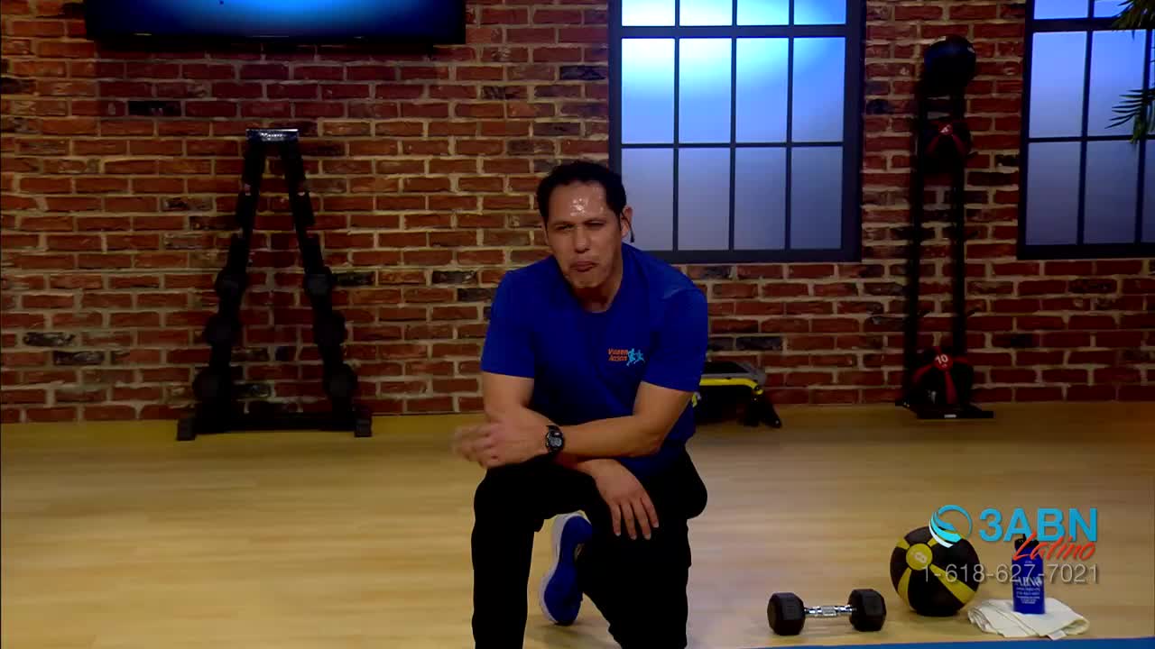 A man in a blue shirt is kneeling on the floor, looking tired. He's on a set for a fitness program, which is broadcast by 3ABN Latino.
