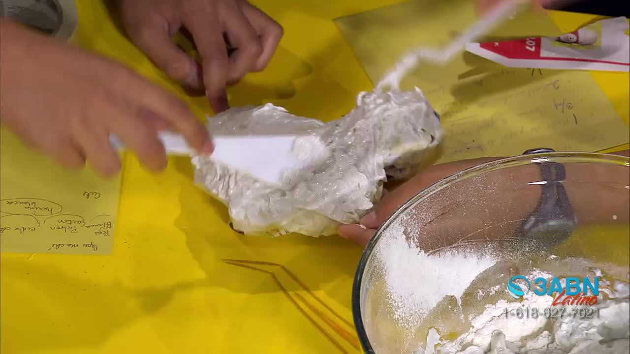 A person is using a spatula to spread a white substance over a form shaped like a creature. Nearby, a bowl of flour sits on the table, and the 3ABN Latino logo is visible.
