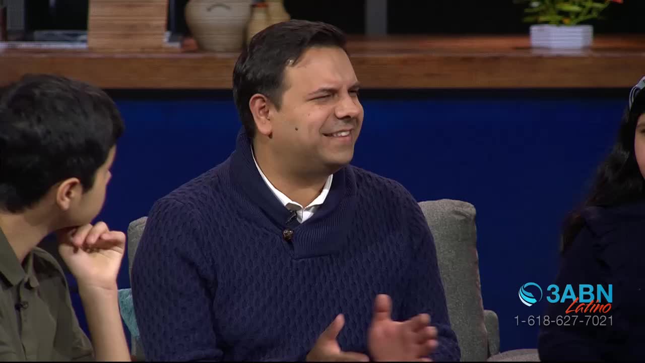 A man in a blue sweater gestures with his hands, smiling at someone off-camera. The 3ABN Latino logo sits in the corner, indicating a broadcast from the United States.
