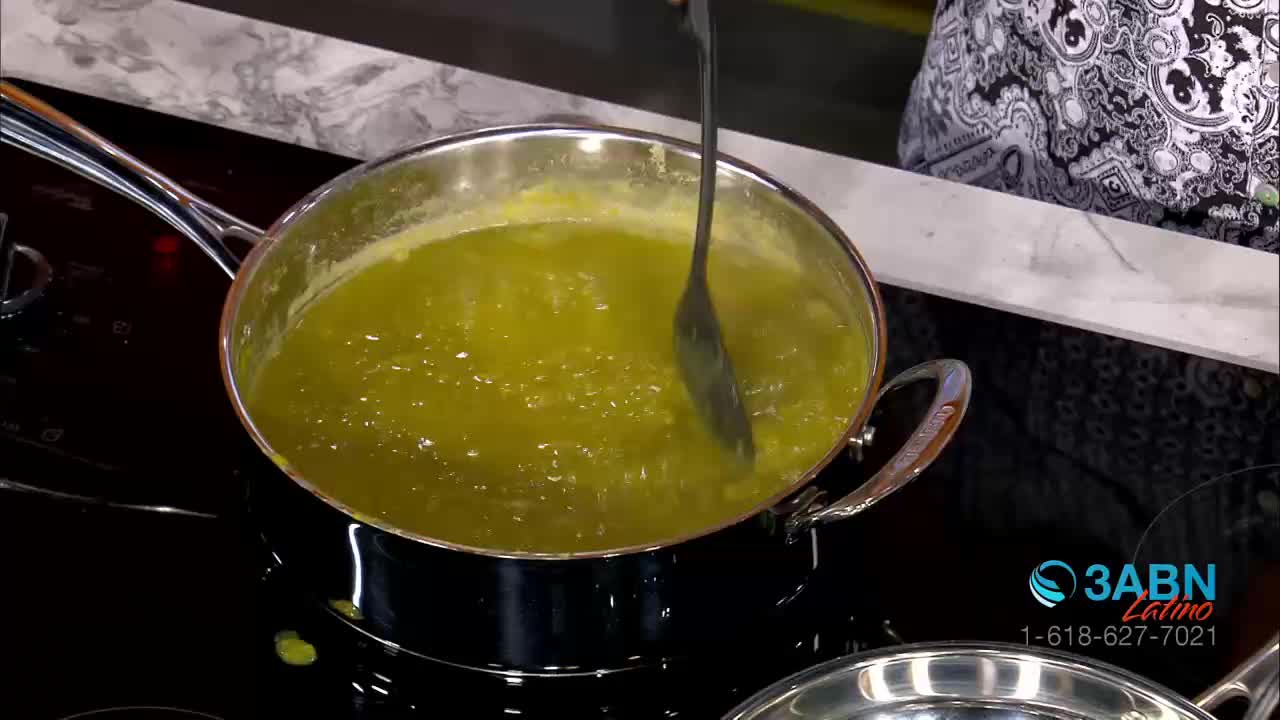 A person stirs a simmering, pale green liquid in a shiny pan on a black stovetop. The 3ABN Latino logo is visible in the corner, indicating a cooking segment.
