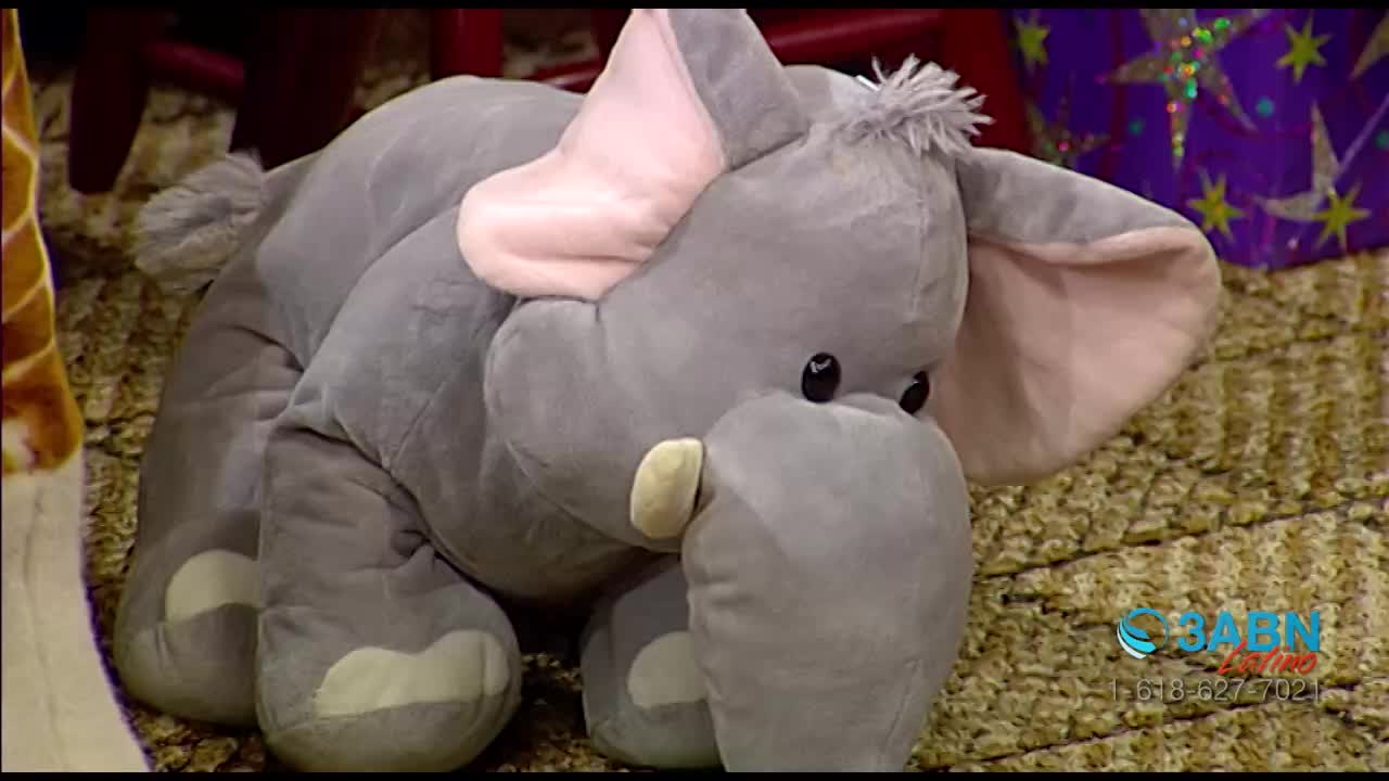 A large, plush elephant sits on a patterned rug, its gray body contrasting with the pink of its ears. The 3ABN Latino logo is visible in the bottom right corner.
