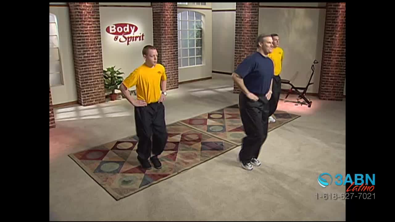 Three men in workout clothes are jogging in place on a patterned rug. The man in the blue shirt is leading the group, with his hands on his hips.
