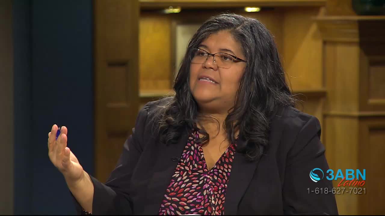 A woman with glasses and long, dark hair gestures with her right hand while speaking. Behind her, the 3ABN Latino logo is visible.
