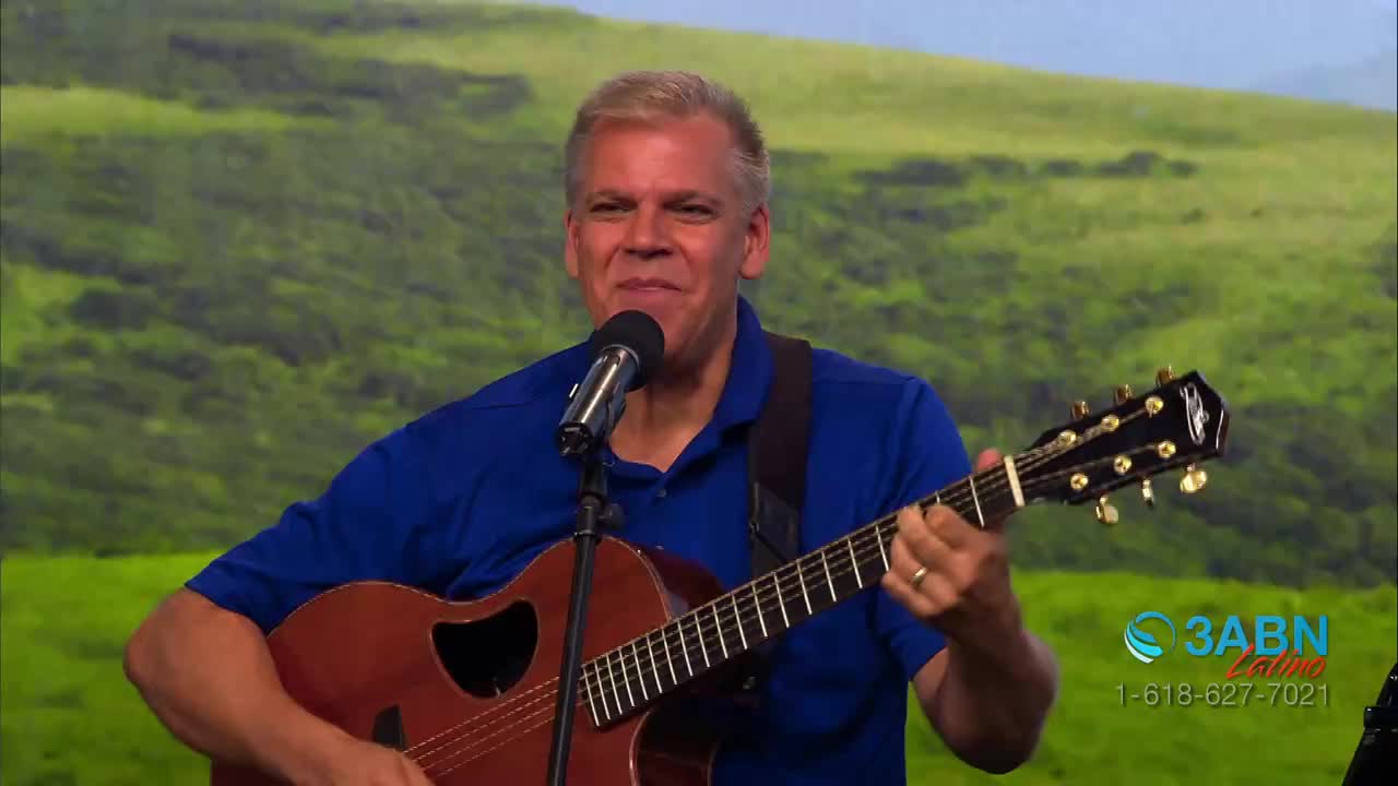 A man in a blue shirt strums an acoustic guitar, singing into a microphone. The 3ABN Latino logo is visible in the corner of the shot.
