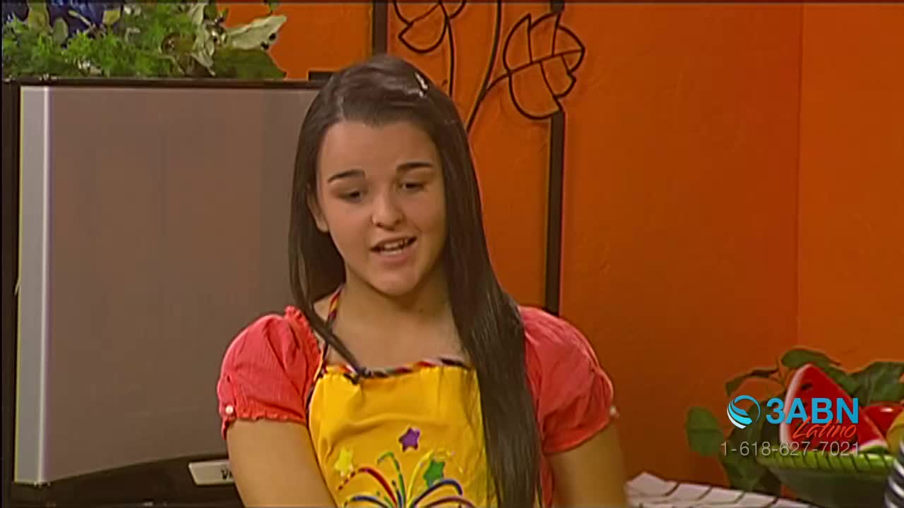 A young woman in a red-sleeved top and a yellow apron is speaking, possibly on a cooking show. The 3ABN Latino logo is visible in the corner.
