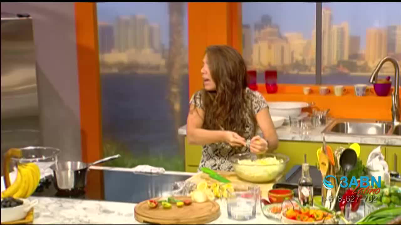 A woman, on a set for 3ABN Latino in the United States, is preparing food, focused on something in a bowl. She's looking to her left, as if she's talking to someone off-camera.
