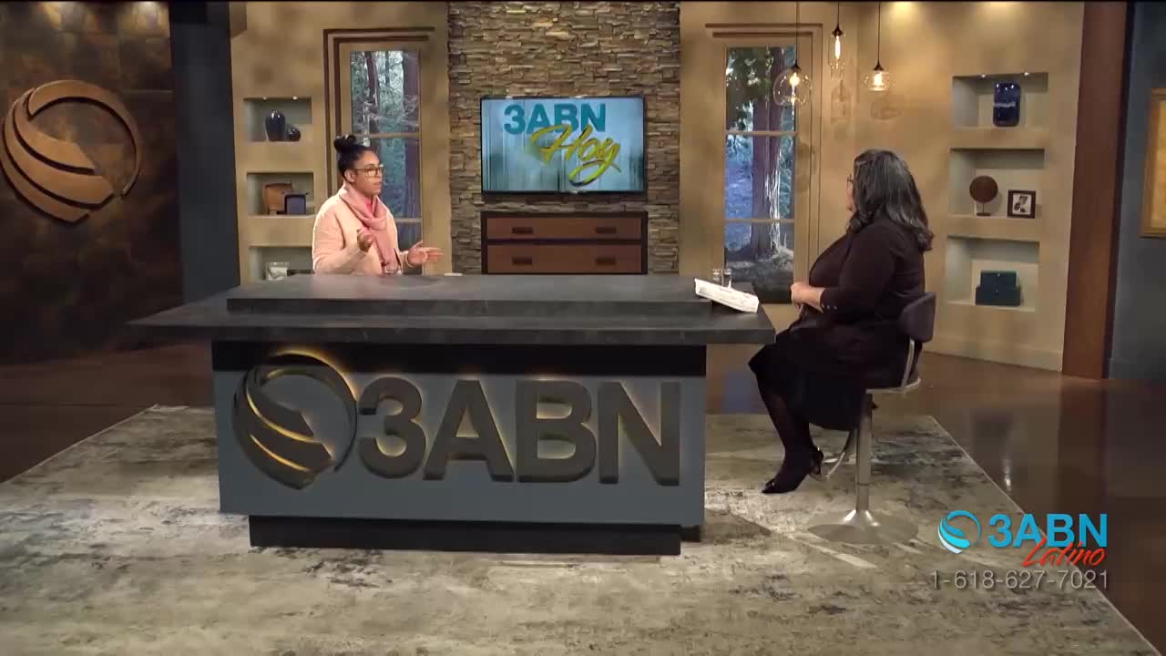 A woman in a pink scarf gestures with her hands as she speaks from behind a desk. Across from her, another woman listens intently, seated in a chair on the set of 3ABN Hoy.
