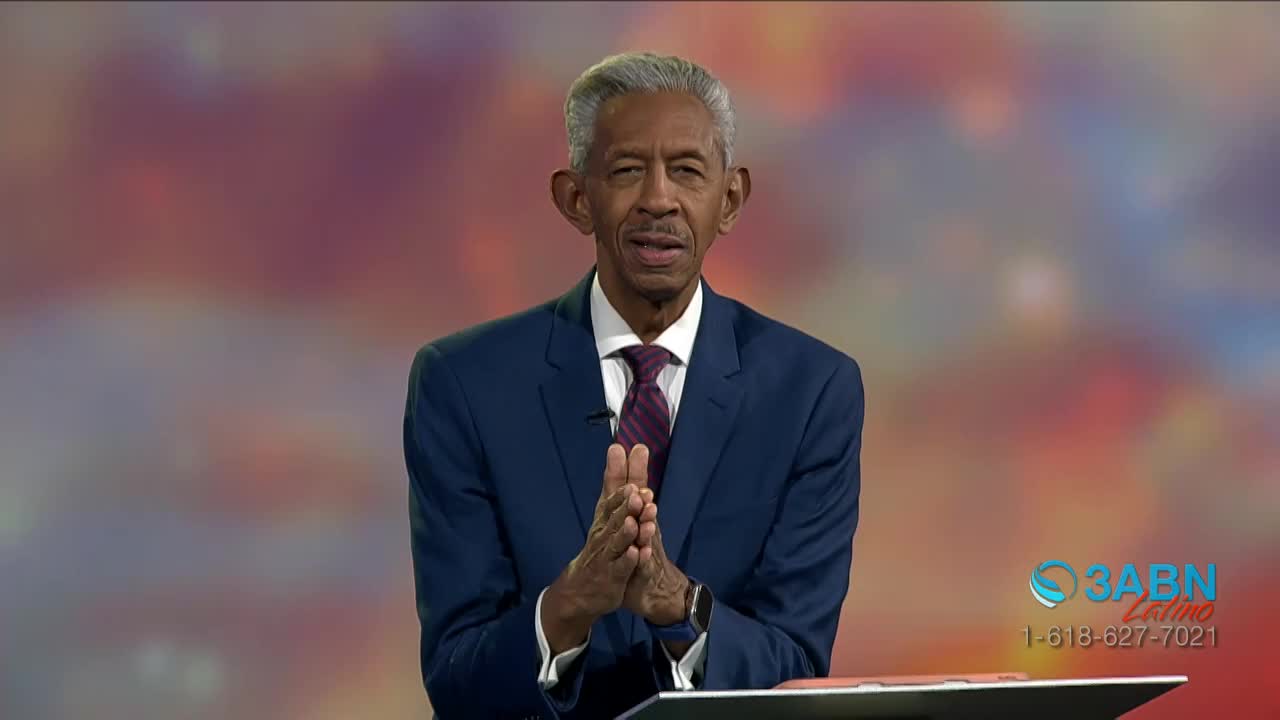 A man in a blue suit stands before a colorful backdrop, his hands clasped together. The 3ABN Latino logo is visible in the corner, with a phone number listed below.
