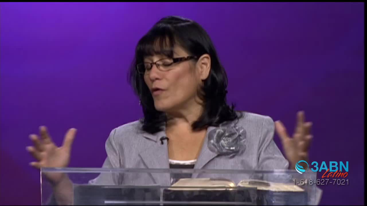 A woman in a gray blazer speaks passionately, gesturing with both hands. Behind her, the 3ABN Latino logo is visible on a purple backdrop.
