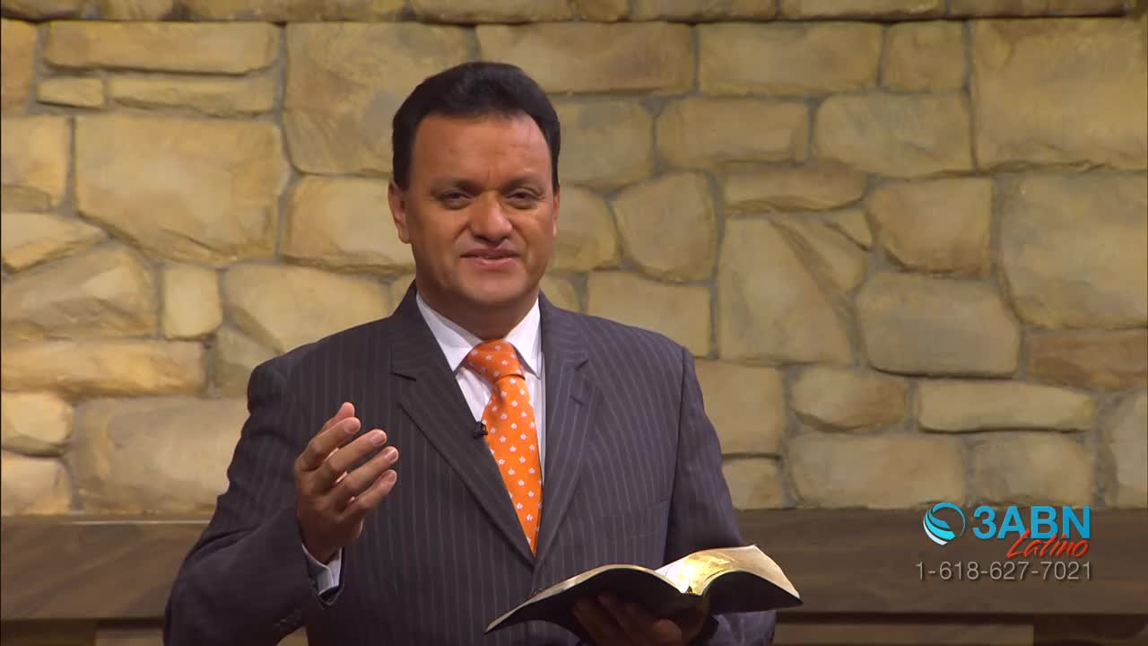A man in a pinstripe suit gestures with his right hand, holding a book in his left. The 3ABN Latino logo is visible in the corner.
