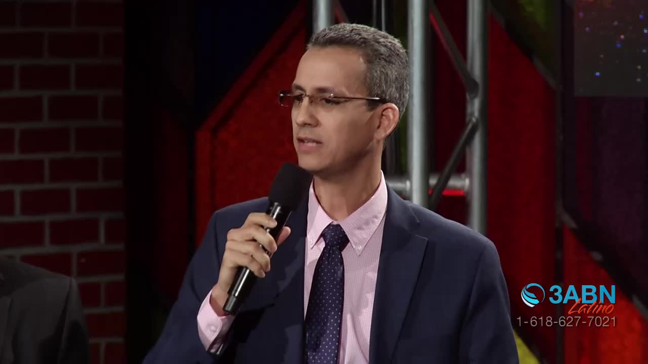 A man in a suit speaks into a microphone, his glasses reflecting the studio lights. The 3ABN Latino logo appears in the corner of the screen.