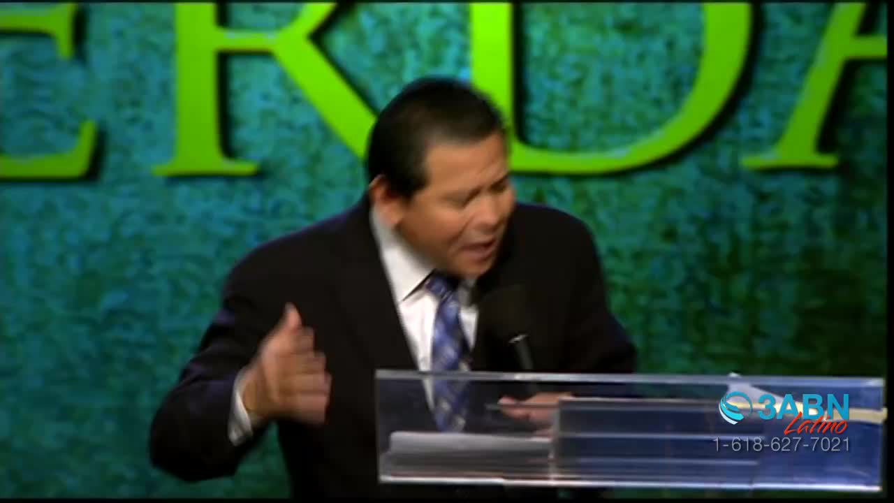 A man in a suit and tie speaks passionately behind a podium. Large green letters on a textured background frame the scene.