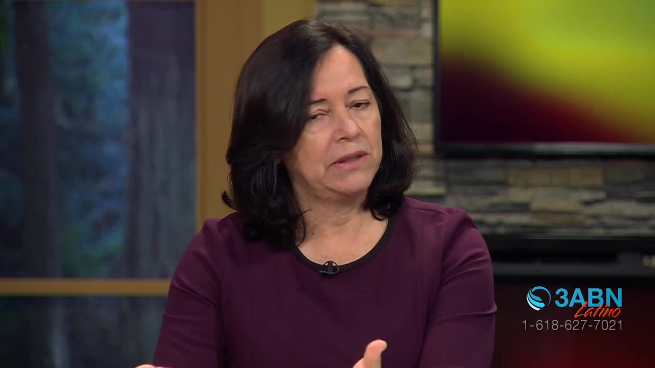 A woman with dark hair speaks, her hands gesturing slightly. Behind her, a screen displays the 3ABN Latino logo and a phone number.