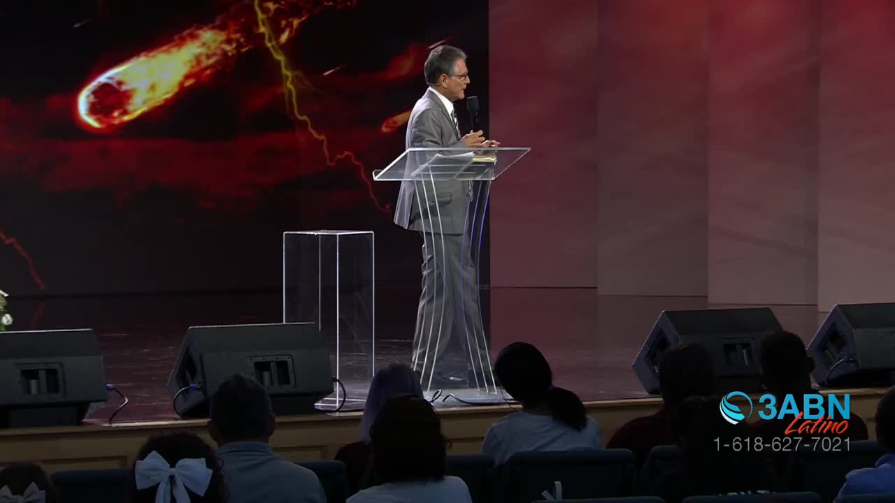 A man in a suit stands at a podium, speaking into a microphone. Behind him, a fiery comet streaks across a dark, red background.