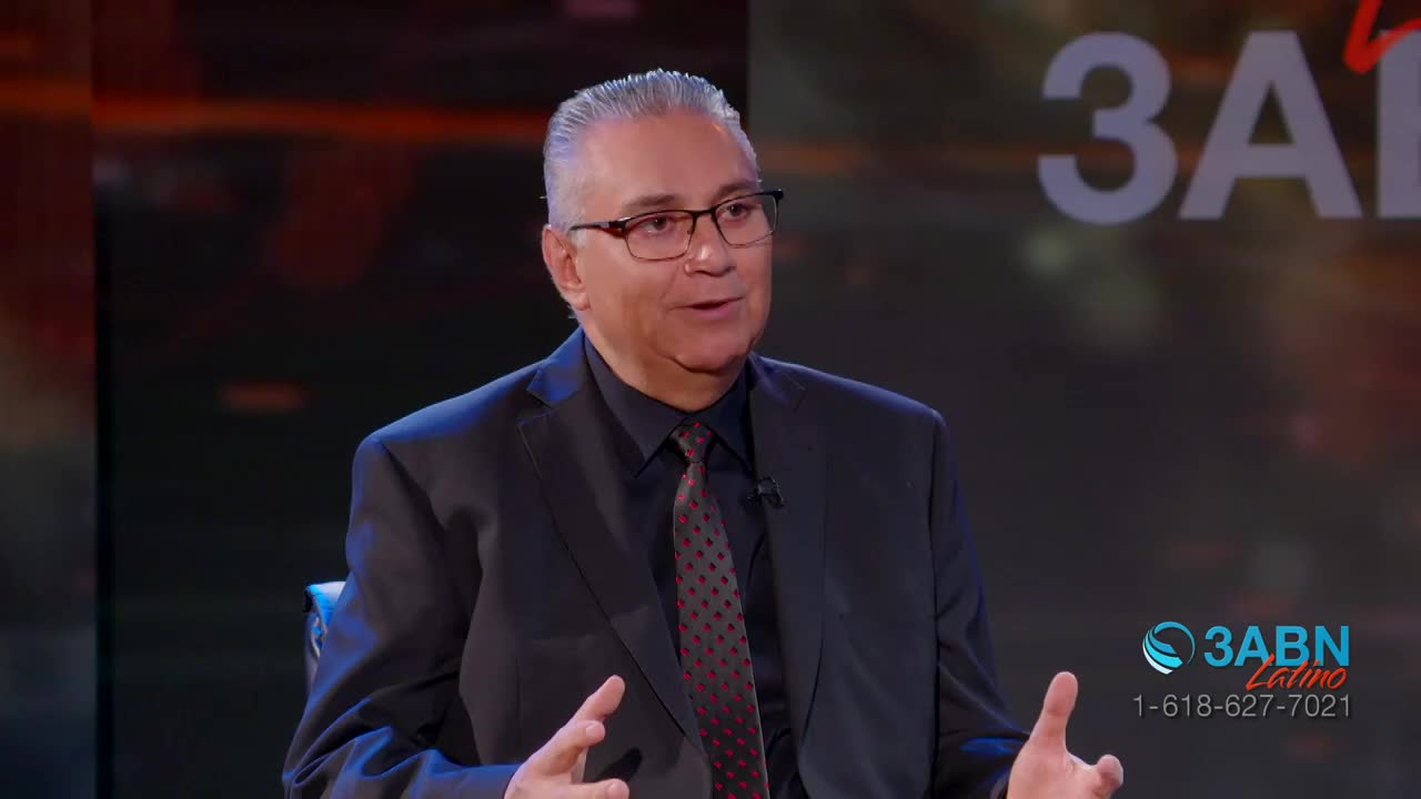 A man in a suit and tie speaks, gesturing with his hands. Behind him, the 3ABN Latino logo glows.