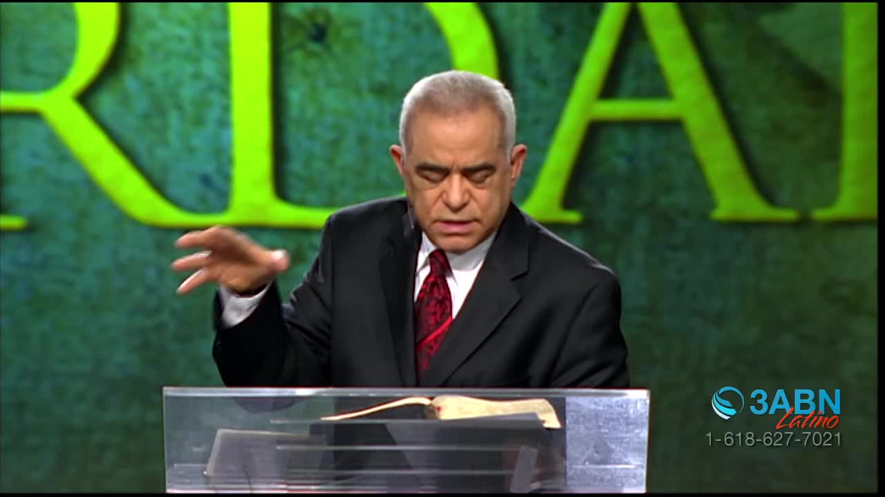 A man in a suit speaks, his left hand gesturing. Behind him, large green letters form part of a word. A logo for 3ABN Latino appears in the lower right corner.