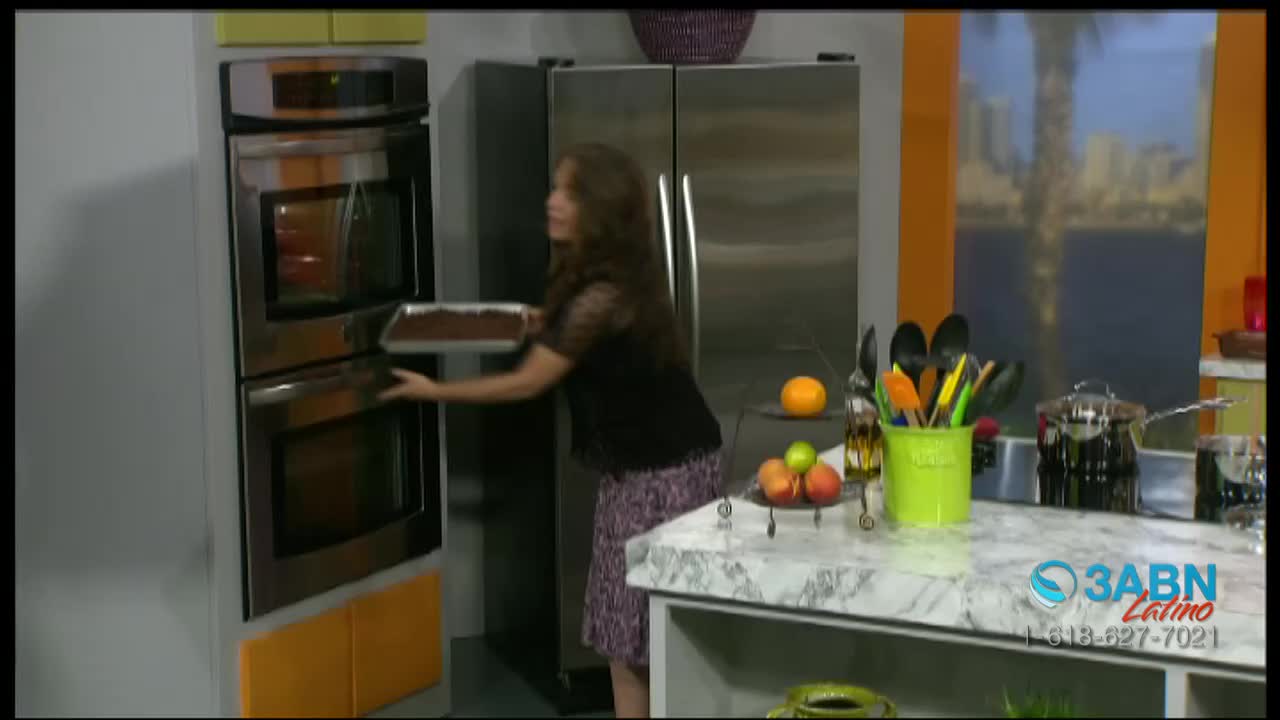 A woman is placing a pan of brownies into a double oven. The 3ABN Latino logo is visible on the counter.