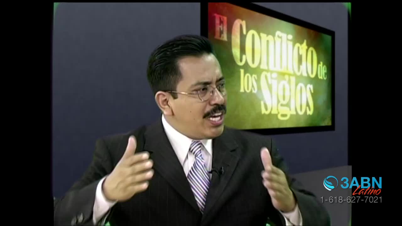 A man in a suit gestures with both hands as he speaks. Behind him, a screen displays the title "El Conflicto de los Siglos" in large, yellow lettering.