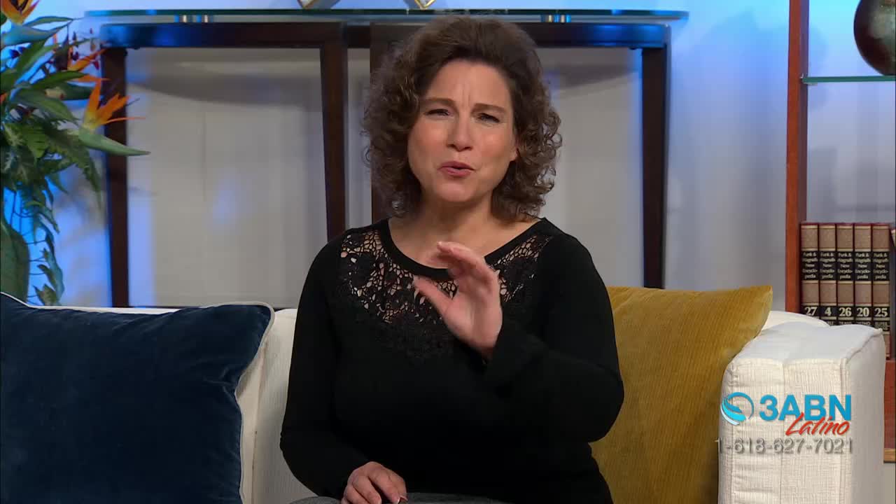 A woman with curly brown hair speaks with her right hand raised, fingers slightly spread. Behind her, a couch is draped with pillows, and a shelf holds a stack of books. A logo for 3ABN Latino appears in the lower right corner.