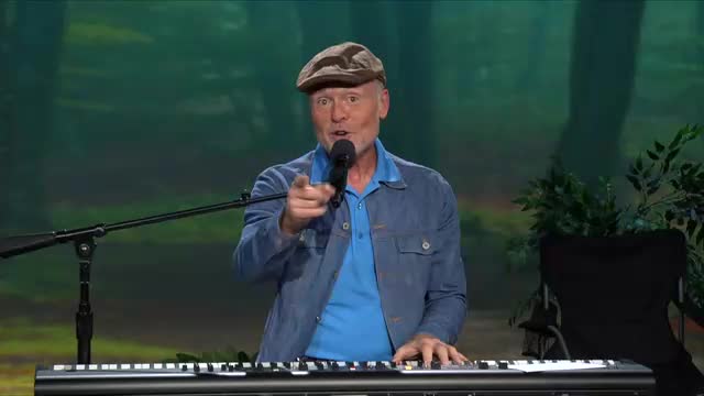 The man in the cap is pointing right at me while singing into a microphone. His fingers are poised above the keys of a keyboard, ready to play.
