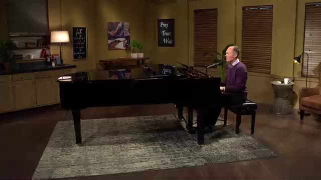 A man in a purple sweater sits at a grand piano, his hands moving across the keys. The scene, likely a studio for 3ABN Praise Him Music Network, is softly lit with a warm, inviting atmosphere.
