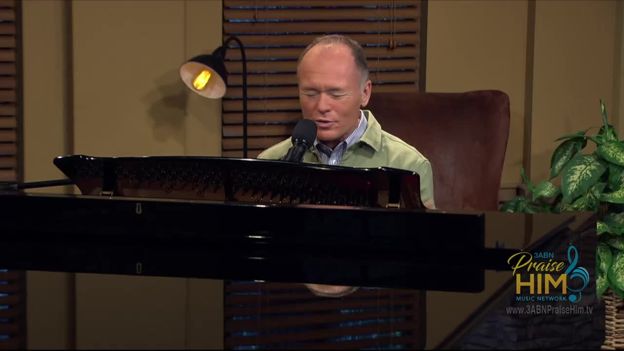 A man in a green shirt sits at a piano, singing into a microphone. The 3ABN Praise Him Music Network logo is visible in the corner.
