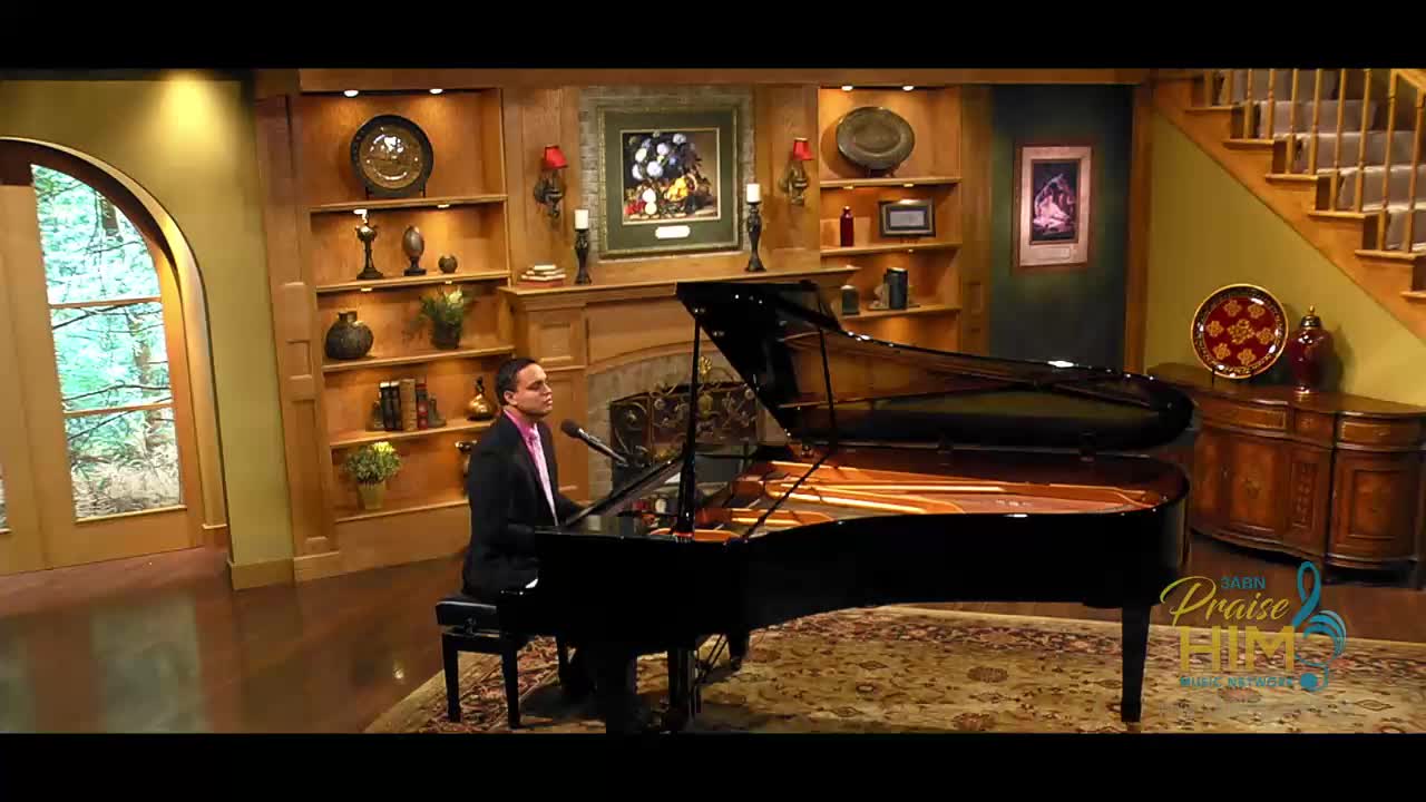 A man in a suit sits at a grand piano, illuminated by soft stage lighting. He's singing into a microphone, and the music fills the room.
