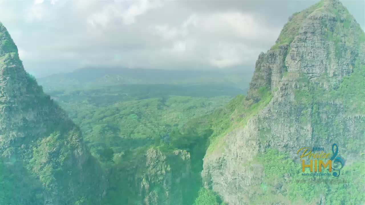 Towering, craggy mountains frame a lush, green valley. The 3ABN Praise Him Music Network logo is visible in the lower right corner.
