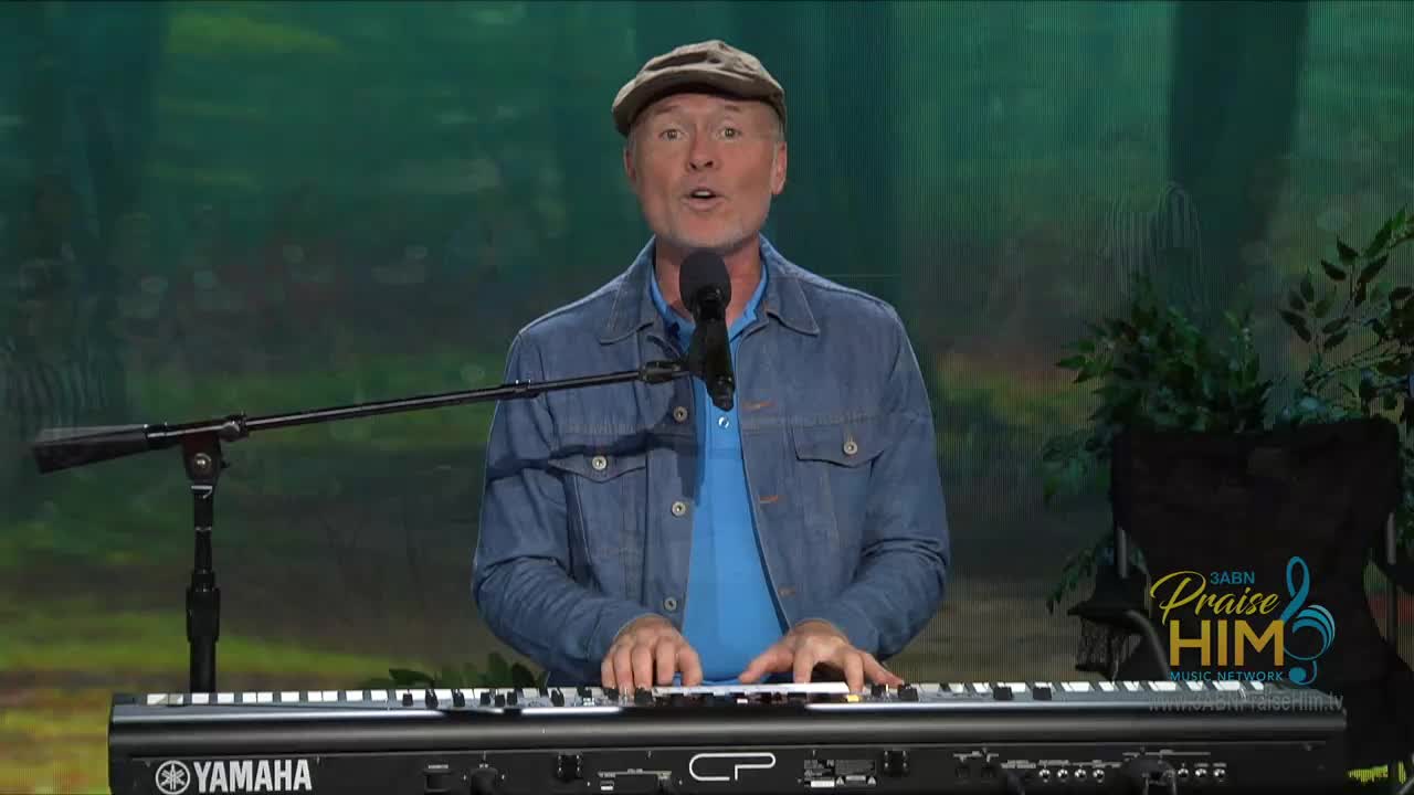 A man in a denim jacket and a cap is playing a keyboard, singing into a microphone. The 3ABN Praise Him Music Network logo is visible in the corner.
