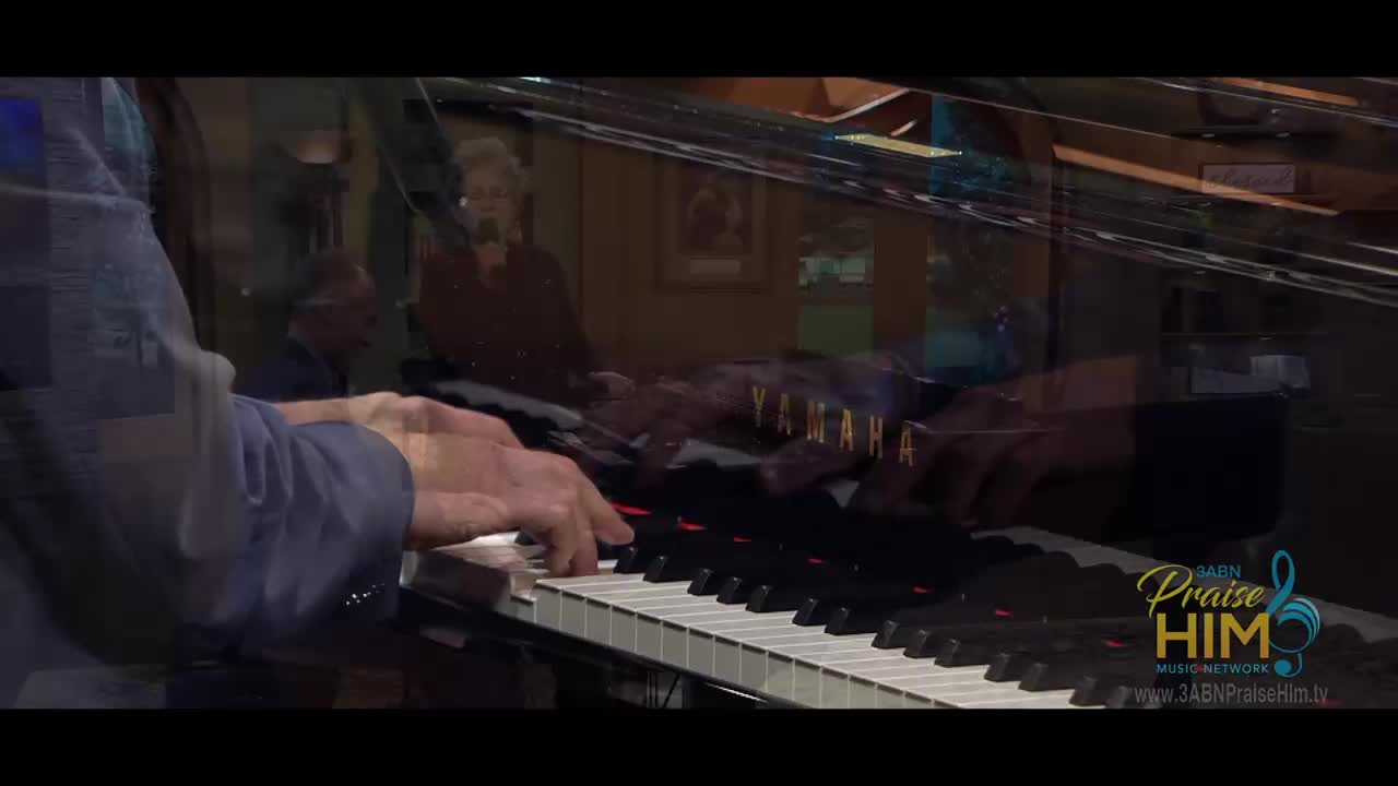 A man's hands are moving across the piano keys, and you can see the Yamaha logo. In the background, a woman sings into a microphone.
