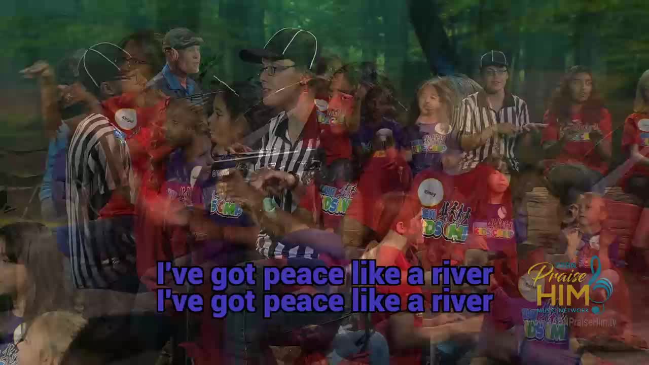 A group of people, some in referee shirts, sing and move in front of a forest backdrop. "Praise Him" is displayed on the screen, as the words "I've got peace like a river" flash below.
