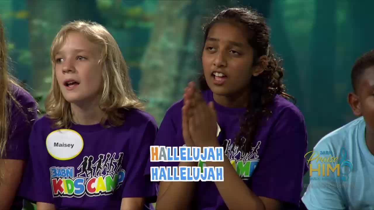 Children in purple shirts are singing, their faces animated. A girl in the center claps her hands, while "Hallelujah" appears on screen.
