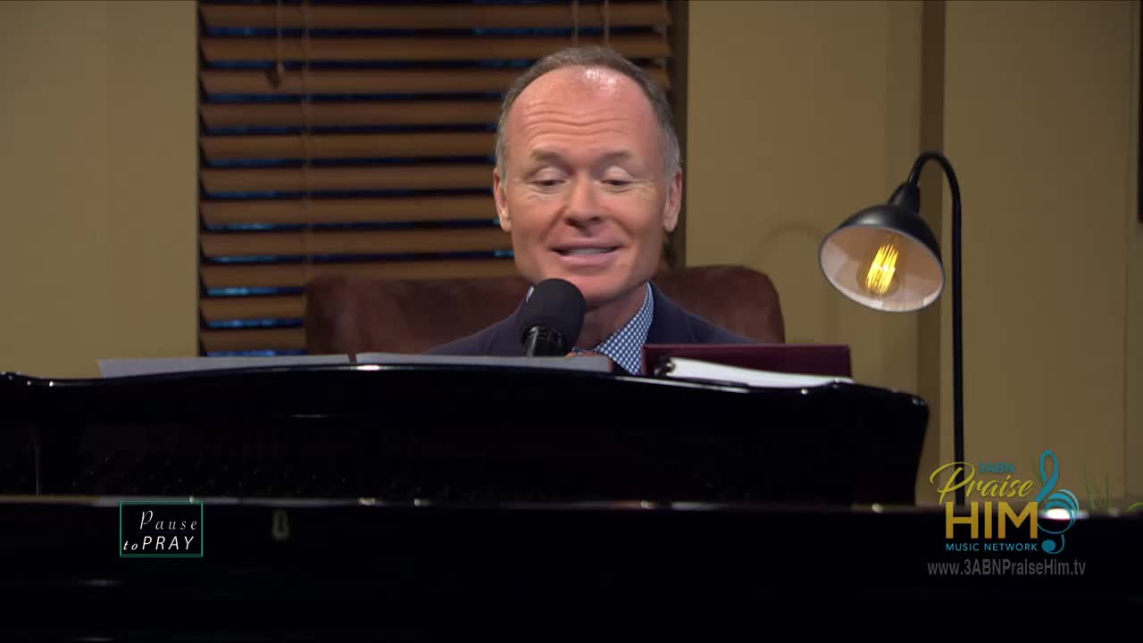 A man sits at a piano, speaking into a microphone. The 3ABN Praise Him Music Network logo is visible on the screen.
