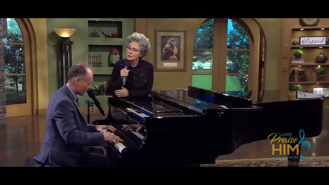 A man in a suit plays the piano, his fingers dancing across the keys. Standing near the piano, a woman sings into a microphone, her eyes closed in concentration.
