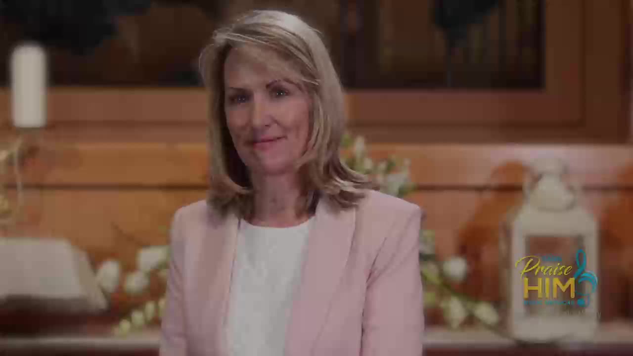 A woman in a pink blazer smiles at the camera, the "Praise Him" logo visible in the background.  She's on the 3ABN Praise Him Music Network, likely in a studio in the United States.
