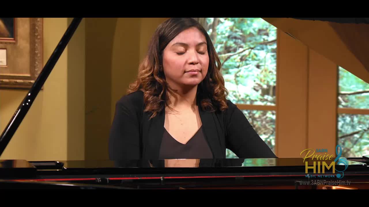 A woman sits at a grand piano, her eyes closed as she plays. The 3ABN Praise Him Music Network logo is visible in the corner.
