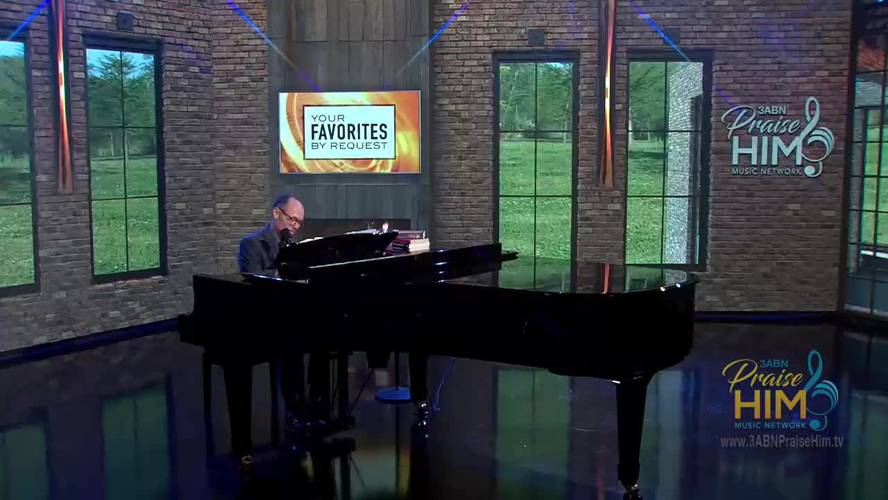 A man in a dark suit sits at a grand piano, playing. Behind him, the 3ABN Praise Him Music Network set features a screen displaying "Your Favorites By Request."
