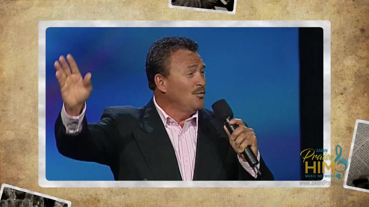 A man in a suit gestures with his right hand as he speaks into a microphone. The 3ABN Praise Him Music Network logo is visible in the corner.
