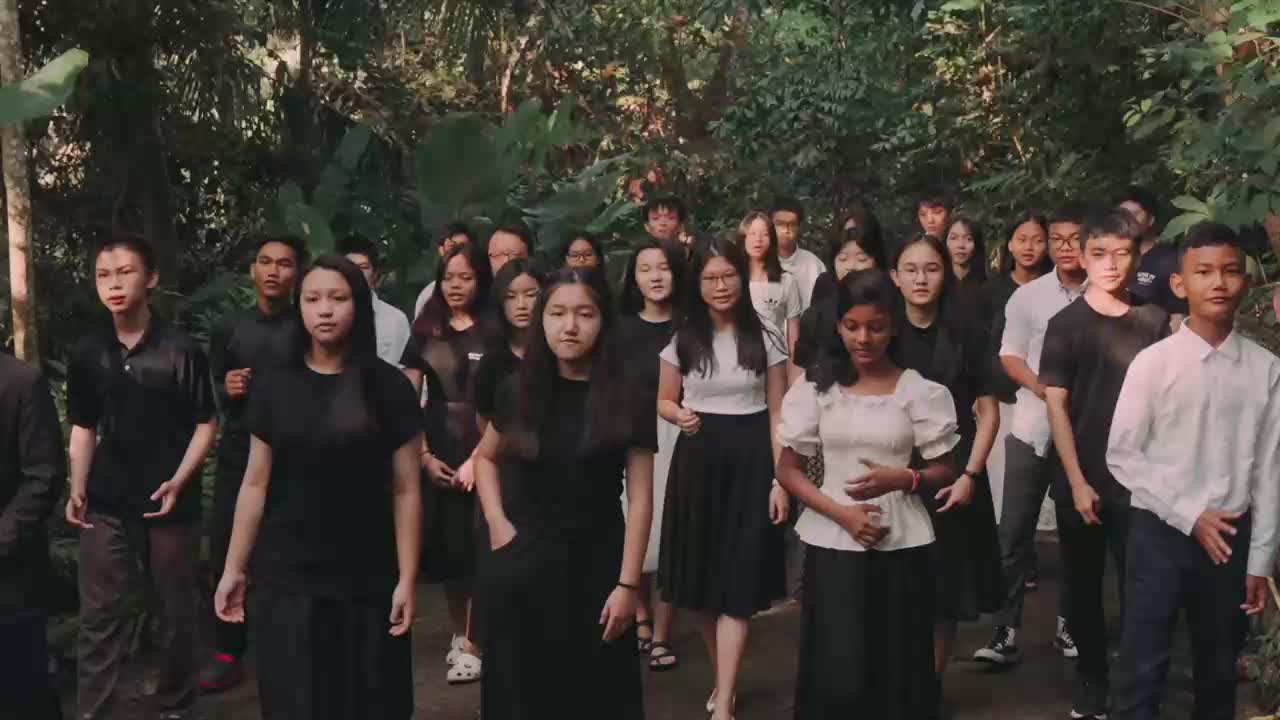 A group of young people, dressed in black and white, walks forward through a lush, green forest. They appear to be heading towards a performance or recording session for the 3ABN Praise Him Music Network.