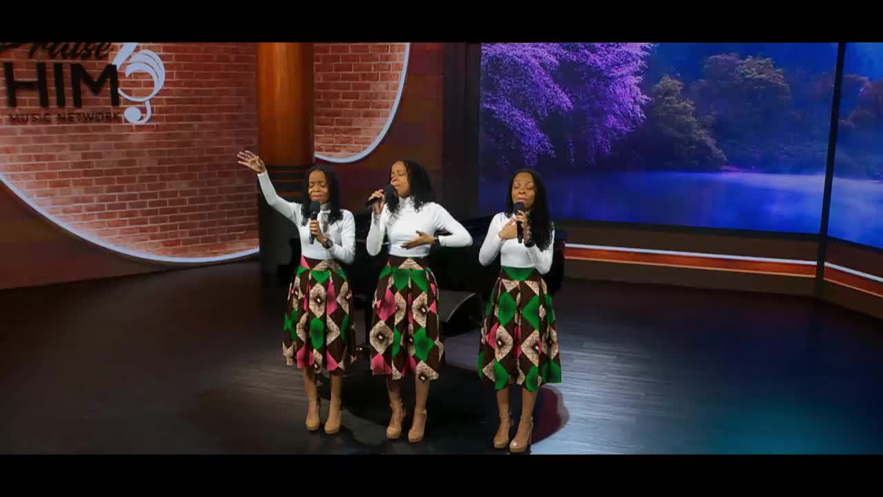 Three women stand on stage, singing into microphones. Their colorful skirts sway slightly as they perform for the 3ABN Praise Him Music Network.
