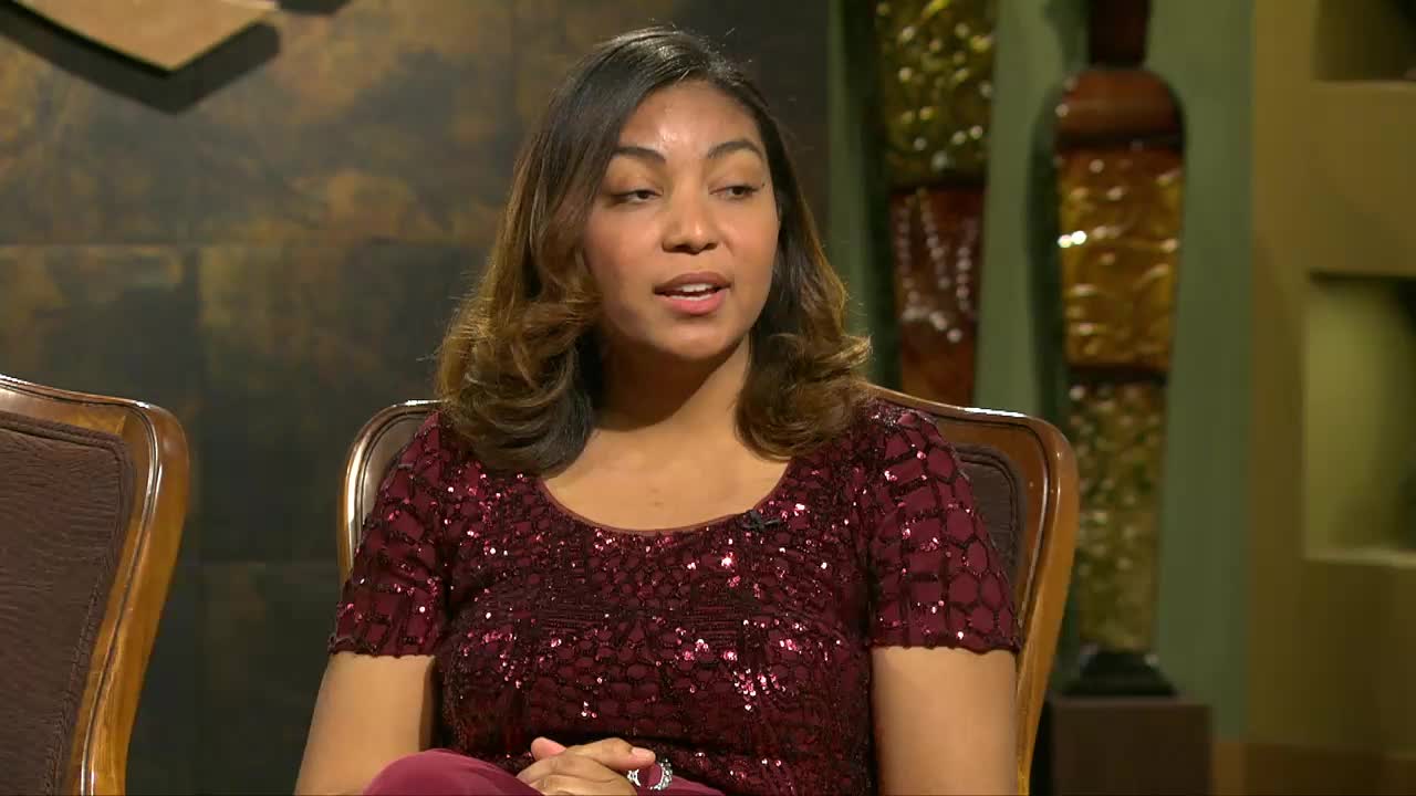 A woman in a sparkling maroon top speaks animatedly, her hands resting in her lap. She's seated in a plush chair, likely during a broadcast for the 3ABN Praise Him Music Network.